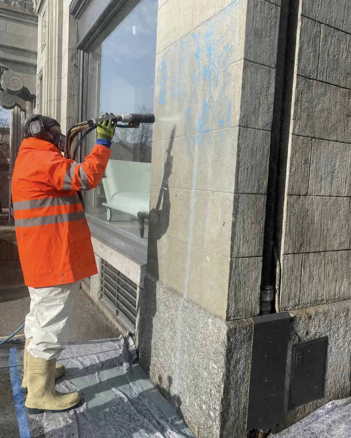 Mitarbeiter von Der Abdichter entfernt Graffiti von einer Natursteinfassade, mit Atemschutz und Strahlgerät